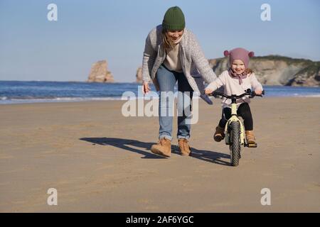 Mère d'exécution à côté de jeune fille vélo on beach Banque D'Images
