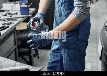 Close up de processus de travail de mécanicien auto portant des gants de protection en caoutchouc et en uniforme bleu garage. Maintien de la vieille bougie d'réparateur et la pulvérisation s Banque D'Images