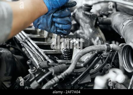 Close up of man's hands dans la poussière des gants en caoutchouc en maintenant le tournevis et serrer les boulons dans l'bougies de moteur de voiture. L'entretien, de diagnostic et de repar Banque D'Images