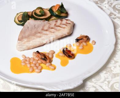 Poisson grillé steak avec des moules. Close up griller un filet de poisson avec légumes et sauce à l'orange décoré de cedre écrous sur la plaque blanche. Banque D'Images