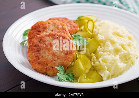 Des escalopes poêlées/boulettes avec de la purée de pommes de terre et cornichon sur plaque blanche. Banque D'Images