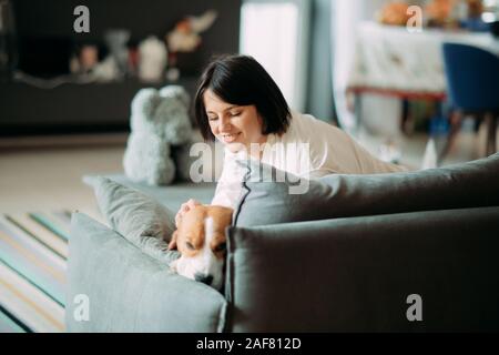 Une femme se trouve sur un canapé à côté d'un chien beagle et les embrassades lui. Banque D'Images