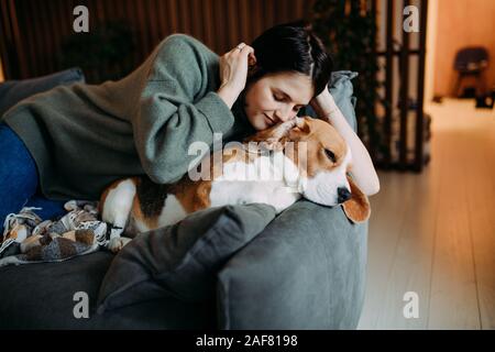 Une femme se trouve sur un canapé à côté d'un chien beagle. Banque D'Images