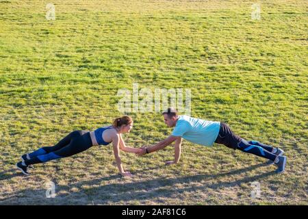 Jeune couple de mettre en place les sportifs boy and girl doing exercise sur l'herbe verte de l'extérieur du stade. Banque D'Images