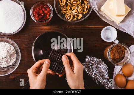 Processus de cuisson brownie fait maison, vue du dessus. Woman's hands break bar de chocolat noir dans la casserole pour faire fondre et faire de la pâte à gâteau délicieux. Banque D'Images
