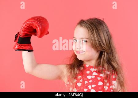 Kid avec bras flexible, muscle biceps, triceps dans des gants de boxe. Boxer enfant aux cheveux longs sourire sur fond rouge. Girl power, le féminisme concept. Le sport, l'énergie, de l'activité. La lutte pour l'amour. Banque D'Images