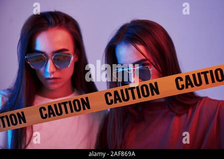 Attention, danger, ruban adhésif jaune. Studio shot à l'intérieur avec lumière néon. Photo de deux magnifiques jumeaux Banque D'Images