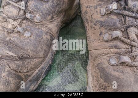 Fermer coup de lacets boueux et œillets sur paire de bottes de randonnée avec des vieilles feuilles au sol. Métaphore camping, randonnée / trekking, vie en plein air Banque D'Images