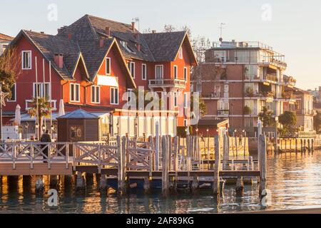 Le front de mer de Lido, Venise, Vénétie, Italie au coucher du soleil avec restaurant rouge coloré et les immeubles à appartements. Jetée en bois de ferry en premier plan. Banque D'Images