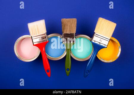 Quatre pots de peinture avec des pinceaux sur fond bleu. Jaune, bleu, rose, turquoise couleurs de peinture. Vue d'en haut. Banque D'Images