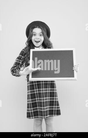 Présentation de produit. petite fille en français beret. bonne fille avec les cheveux bouclés beret. publicité. enfant avec tableau noir vide. enfant sur jaune. copie espace. Les heures d'école. présentation de projet scolaire. Banque D'Images