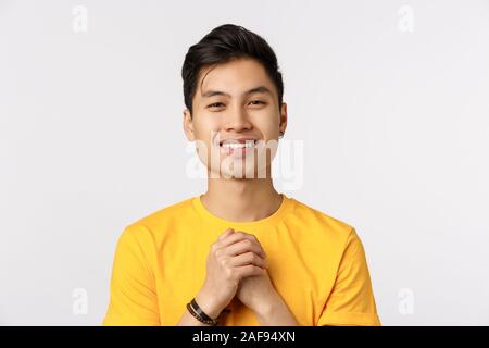 Close-up shot reconnaissant, cute guy hipster chinois en t-shirt jaune, serrez les mains sur la poitrine en reconnaissant ou touché posent, souriant heureux Banque D'Images