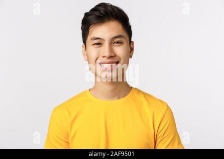 Gros plan homme asiatique avec enthousiasme joyeux pierced oreille, porter des t-shirt jaune, souriant sourire rayonnant, exprimer des émotions positives, optimistes Banque D'Images