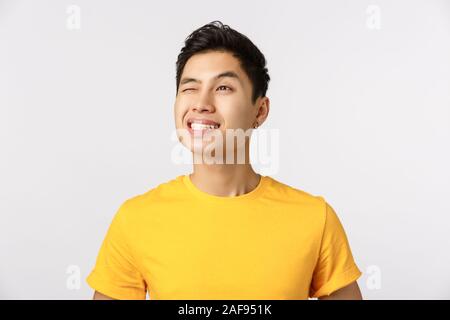 Gai et beau rêve chinois en jaune t-shirt, un sourire ravi, avec un clin d'envisager à loucher ou beau soleil, voir la lumière du soleil Banque D'Images