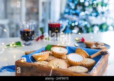 Composition de confortable chaud gentil anglais fête traditionnelle pâtisserie mince pies en plateau en bois avec du vin et des boissons lights garland sur accueil table wi Banque D'Images