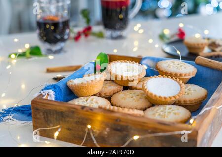 Composition de confortable chaud gentil anglais fête traditionnelle pâtisserie mince pies en plateau en bois avec du vin et des boissons lights garland sur accueil table wi Banque D'Images