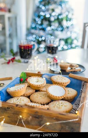 Composition de confortable chaud gentil anglais fête traditionnelle pâtisserie mince pies en plateau en bois avec du vin et des boissons light garland sur accueil table wit Banque D'Images