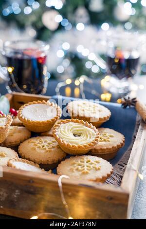 Composition de confortable chaud anglais fête traditionnelle pâtisserie mince pies en plateau en bois avec arrière-plan flou de vin chaud des boissons, une guirlande de feux Banque D'Images