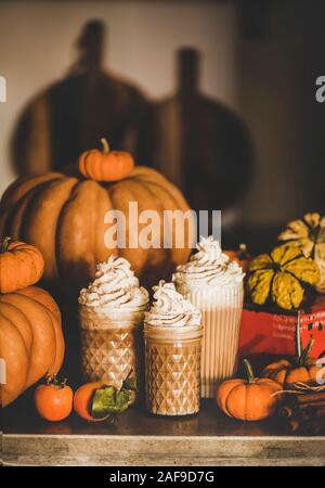 Boire du café latte épicé à la citrouille garnie de crème fouettée dans des verres frais parmi les citrouilles, les kakis et les bâtons de cannelle sur le comptoir de la cuisine. Seasona Banque D'Images
