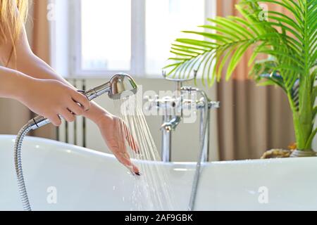 Verse de l'eau hors de la douche sur le girl's hands. Sur un fond bleu. Femme vérifie la température de l'eau dans le fond de la salle de bains Banque D'Images