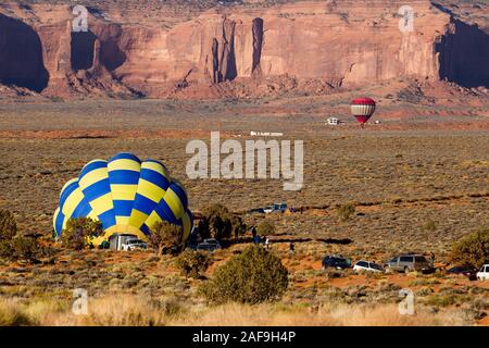 Une équipe gonfle un ballon chaud en préparation du lancement dans le Monument Valley Navajo Tribal Park en Arizona. Un autre ballon est takinf off dans la ba Banque D'Images