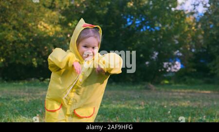 Une petite fille dans une danse raindance jaune sur la pelouse. Elle est en attente de la pluie. Banque D'Images