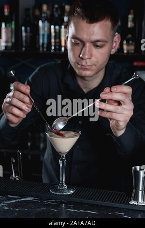 Bartender making Espresso martini cocktail, finishig en ajoutant des grains de grenade sur le dessus. Bar sur un arrière-plan. Banque D'Images