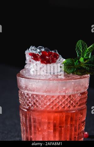 Cocktail froid avec de la glace et de grenat, morceau de graines de grenade, Derrière sur fond sombre Banque D'Images