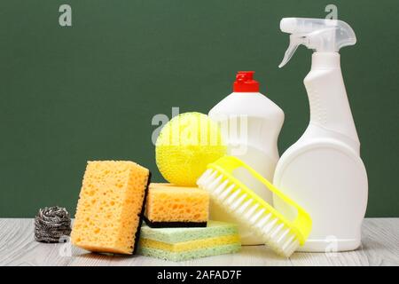 Les bouteilles en plastique de liquide vaisselle, verres et tile cleaner, pinceau et éponges jaune sur fond vert et de sol stratifié. Le lavage et l'cleanin Banque D'Images