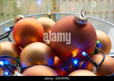 Un bol en verre mat de couleur orange bronze chtristmas et boules de lumières de Noël multicolores devant une fenêtre. Banque D'Images