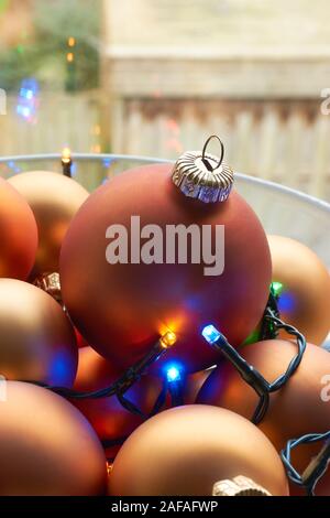 Un bol en verre mat de couleur orange bronze chtristmas et boules de lumières de Noël multicolores devant une fenêtre. Vertical image. Banque D'Images