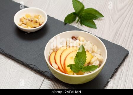 Avec Bol en porcelaine avec de la bouillie de sorgho peach, noix de cajou et amandes, bol avec les écrous à l'office de pierre. Sans gluten vegan salade de sorgho avec fre Banque D'Images