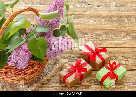 Panier en osier avec lilas fleurs et feuilles vertes, les coffrets cadeaux avec des rubans sur les anciennes planches de bois. Vue d'en haut. Banque D'Images