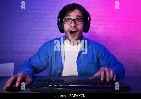 L'homme surpris à jouer en ligne jeu d'ordinateur, wearing headset Banque D'Images