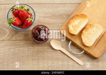 Confiture de fraises faites maison et les baies fraîches dans bols en verre, d'un toast sur une planche à découper avec cuillère sur un bureau en bois. Vue d'en haut. Banque D'Images