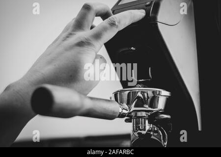 Un portrait d'un barista en appuyant sur le bouton d'un moulin à café pour combler un portafilter pleine de grains de café fraîchement moulus à partir de grains de café frais. Banque D'Images