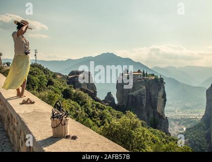 Jeune femme avec robe blanche et grand chapeau debout sur le mur en face de la Grèce, de l'abbaye et de montagnes meteor village de l'arrière-plan Banque D'Images