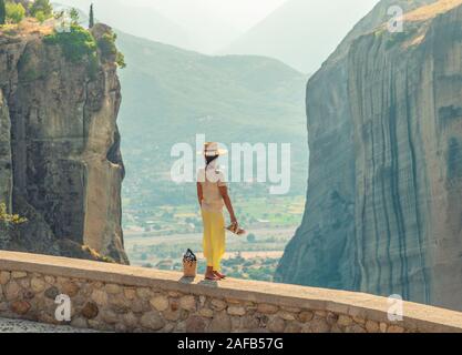 Jeune femme avec robe blanche et grand chapeau debout sur le mur en face de la Grèce, de l'abbaye et de montagnes meteor village de l'arrière-plan Banque D'Images