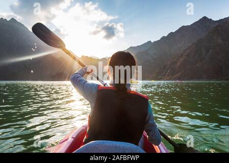 Femme kayak dans un lac entouré de montagne au coucher du soleil Banque D'Images