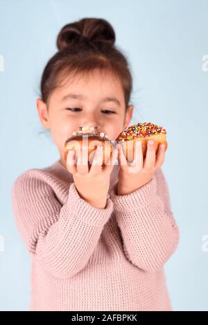 Peu de professionnels cute girl eating donuts sur fond bleu. Enfant s'amusant avec anneau. Banque D'Images