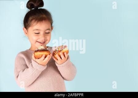 Peu de professionnels cute girl eating donuts sur fond bleu. Enfant s'amusant avec anneau. Banque D'Images