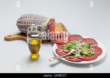 Assiette de tranches de bresaola avec rocket et d'huile d'olive sur un fond blanc Banque D'Images