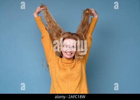 Femme mature à la recherche à l'appareil photo, jouant avec ses longs cheveux blonds. Banque D'Images