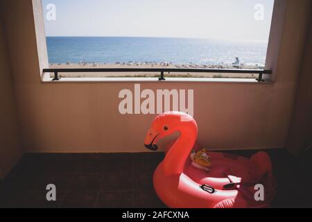 Profondeur de champ (selective focus) avec l'image d'un flamant rose sur la terrasse d'un hôtel et la plage et la mer au premier plan. Banque D'Images