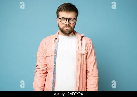 Beau, barbu avec des lunettes réduit un œil et regarde la caméra. Banque D'Images