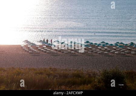 Les gens sur la plage, près de chaises longues et parasols, pelouse tôt le matin au lever du soleil. Banque D'Images