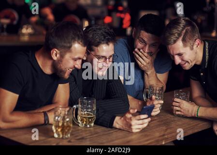 Contenu drôle sur smartphone. Trois amis se reposant dans la pub avec une bière dans les mains. Avoir conversation Banque D'Images