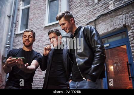Trois amis se trouve à l'extérieur du bar. Avoir une conversation. Dans de beaux vêtements Banque D'Images
