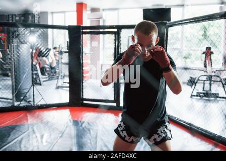 Prêts à se battre. Jeune boxer dans les bandages rouge ont l'exercice. Dans la salle de sport sur la cage Banque D'Images