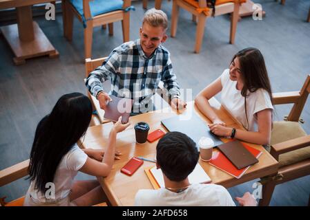 Assis dans un café et avoir une conversation. Quatre jeunes étudiants dans les tenues ont rencontre à jour de pluie Banque D'Images